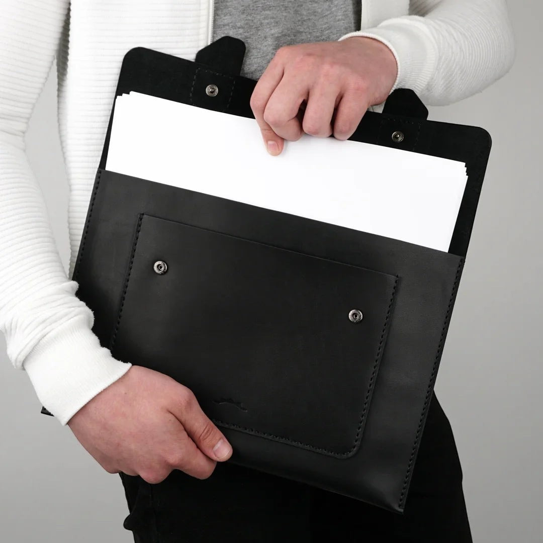 MODISTIAZ black leather document folio with exterior pocket and snap closure, held by a person.