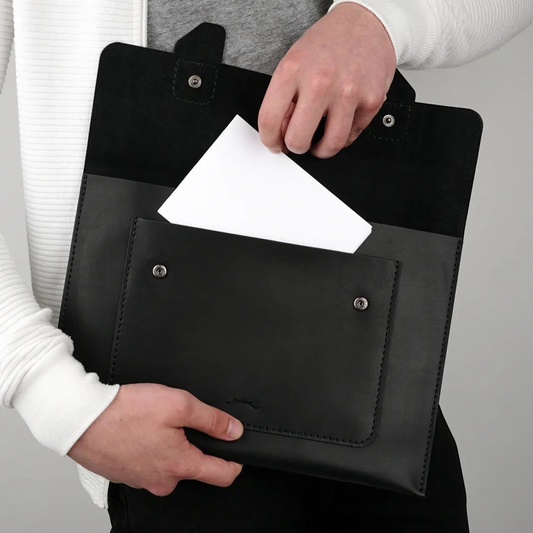 MODISTIAZ black leather document folio with exterior pocket and snap closure, held by a person.
